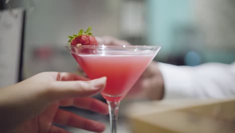 colorful cocktail with a strawberry garnish, bartender hands a drink to a beautiful lady