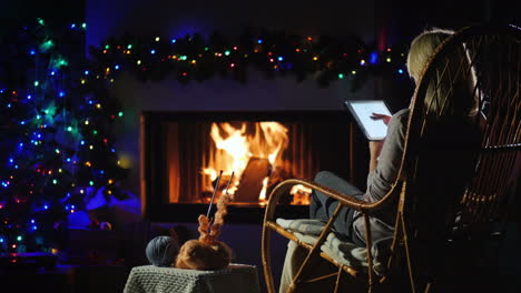 Mujer-Joven-Descansando-Junto-A-La-Chimenea-Usando-Una-Tableta