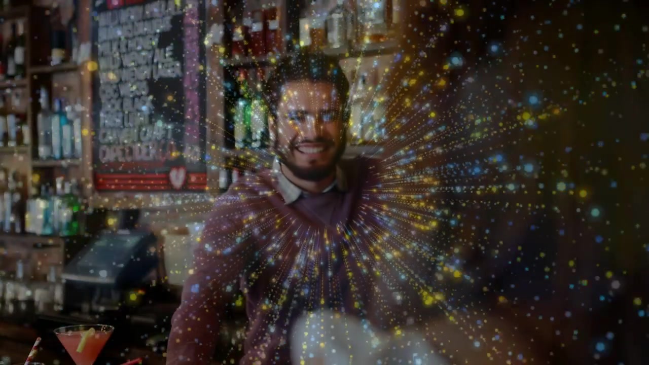 Cliente che alza un dito al bancone del bar, rivelando il barista mentre le scintille si diradano; lui sorride e indica.
