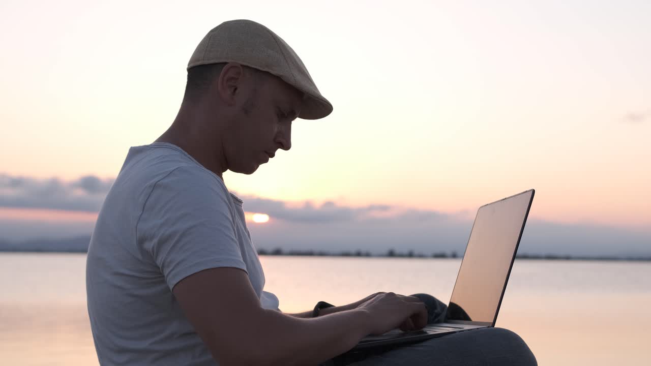 Male traveler sitting on the shore using laptop. Digital nomad or remote worker concept