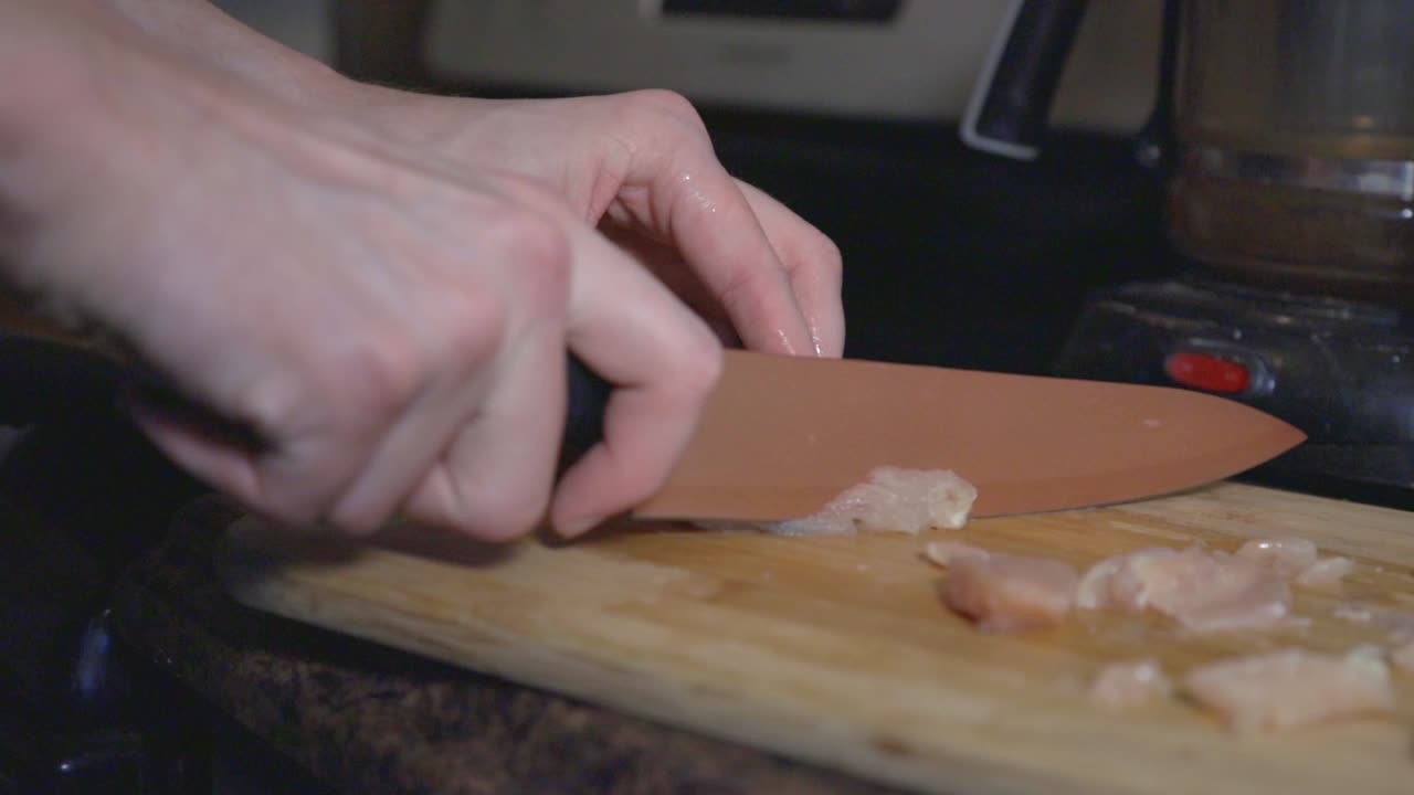 Slicing A Raw Chicken Fillet Using A Kitchen Knife On Wooden Chopping Board. - close up shot