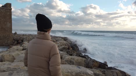 a girl looking out to sea as the waves crash against the rocks