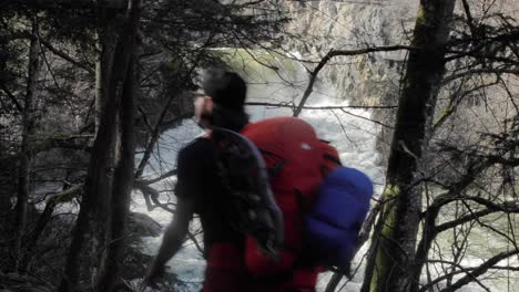 trekking de mochileros masculinos junto a la corriente del río de aguas blancas solo