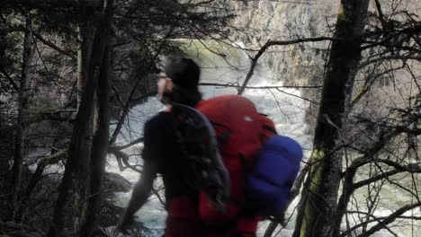 male backpacker trekking next to white water river stream alone