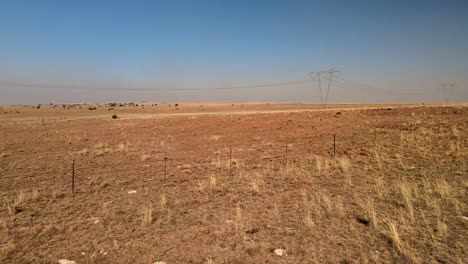 Estructura-De-Línea-Eléctrica-Distante-En-Condiciones-áridas,-Paisaje-Remoto-Y-Desolado-Con-Una-Cerca-Agrícola-Desgastada