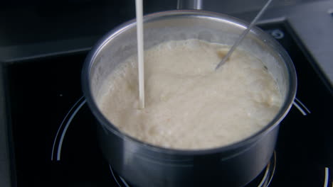 cook mixes sauce by whisk and pours cream in stewpan