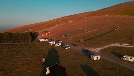 Campervans-And-Vans-Parked-In-Majella-Mountains-Near-The-Ski-Lifts-On-Summer-Morning-During-Sunrise---Aerial-Pull-Back-Drone-Shot