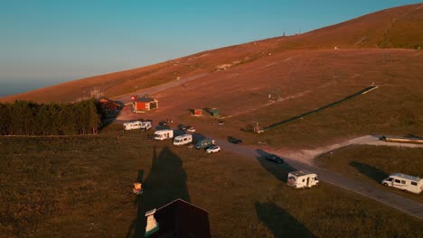 campervans and vans parked in majella mountains near the ski lifts on summer morning during sunrise - aerial pull back drone shot