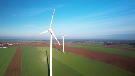 Aerial-View-Of-Pair-Of-Wind-Turbines-With-Spinning-Propellers-In-Green-Field