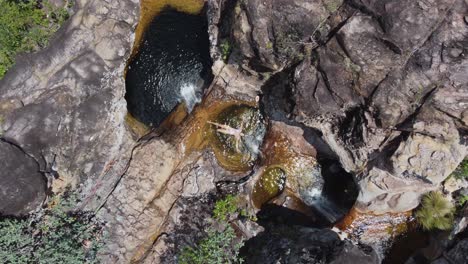 aerial descends to woman in small pothole waterfall pool in bolivia