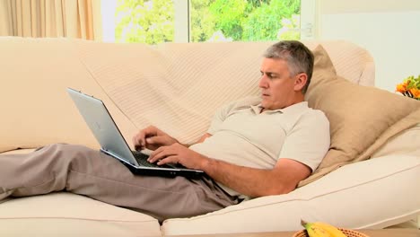 Man-lying-on-coch-working-on-his-laptop