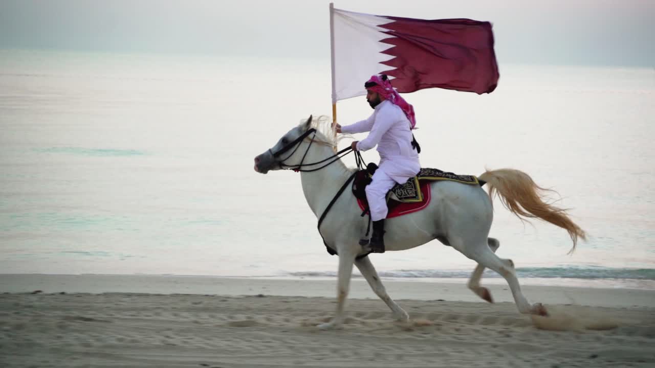 un caballero montando un caballo corriendo y sosteniendo la bandera de qatar cerca del mar-2