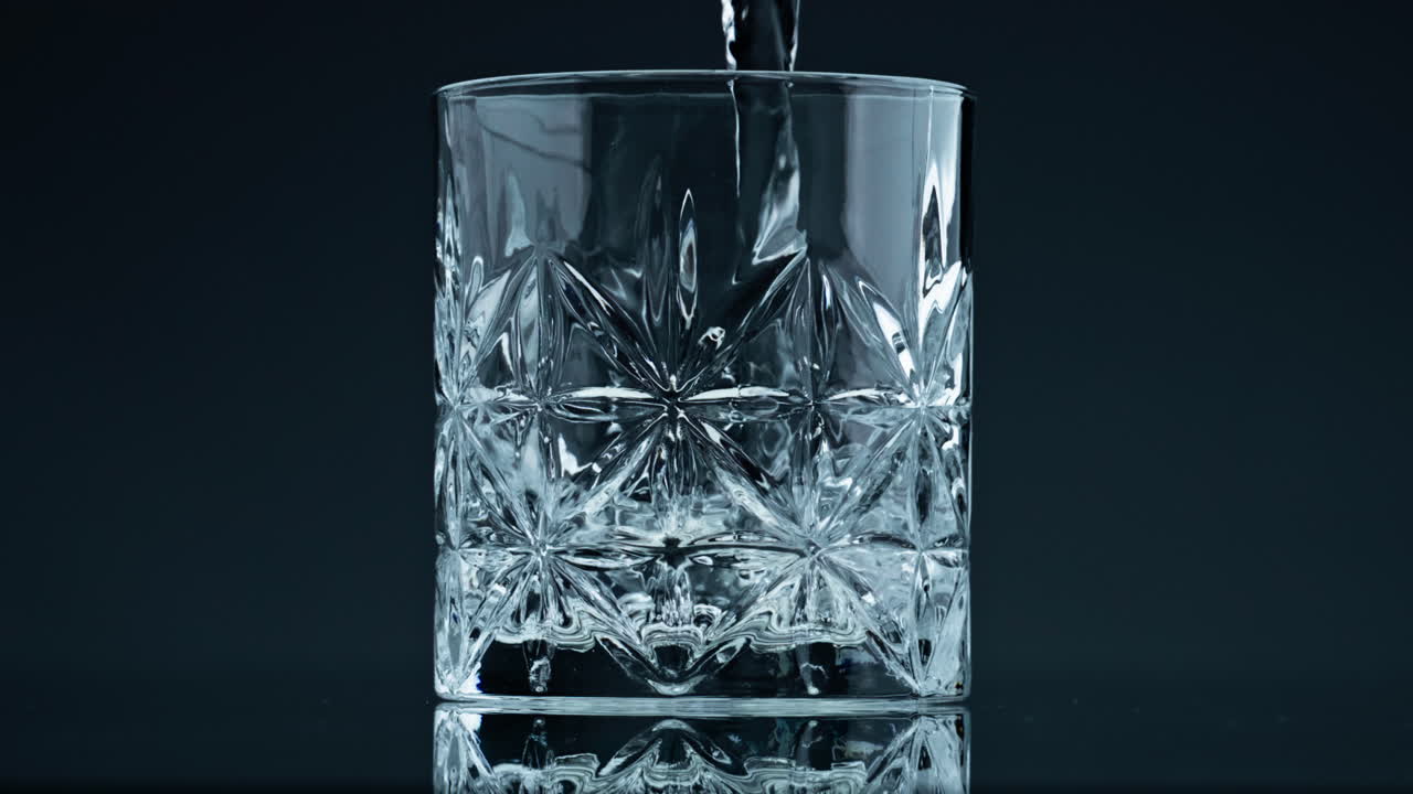Crystal water pouring glass at dark background closeup. Fresh liquid splashing