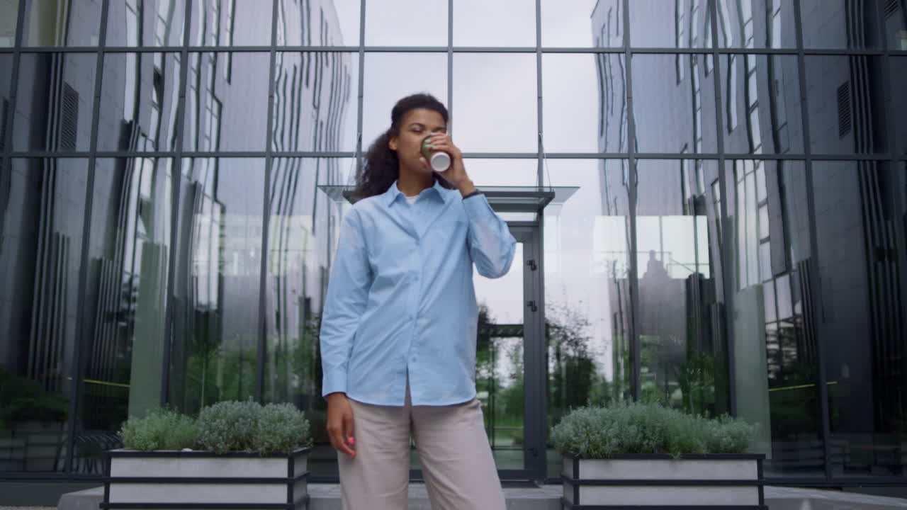 Pleased businesswoman posing drinking coffee cup on contemporary office facade.