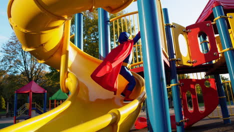 child in superhero costume on playground slide