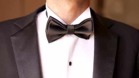 the groom in the black suit adjusts his bow tie of the white shirt - close up