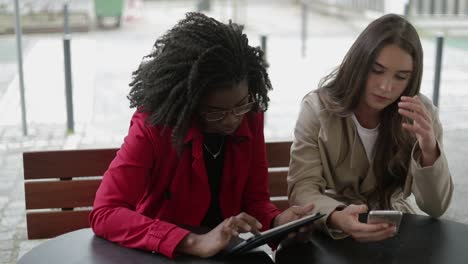 Two-women-swiping-photos-on-gadgets,-looking-serious-and-upset