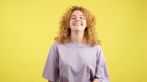 joyful young woman with curly hair smiling on yellow background