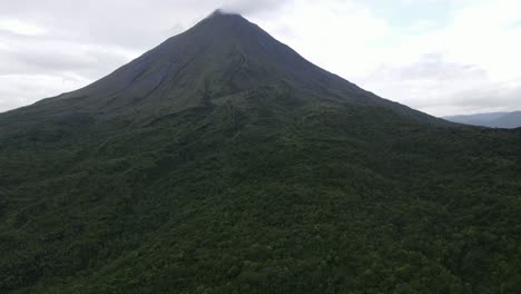 Toma-Ascendente-De-Vista-Aérea,-Vista-Panorámica-Del-Volcán-Arena-En-Costa-Rica,-Nube-En-La-Punta-Del-Volcán-Y-Cielo-Azul-Brillante-En-El-Fondo