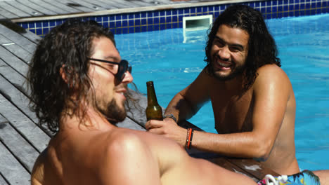 amigos felices interactuando entre sí mientras disfrutan de bebidas junto a la piscina