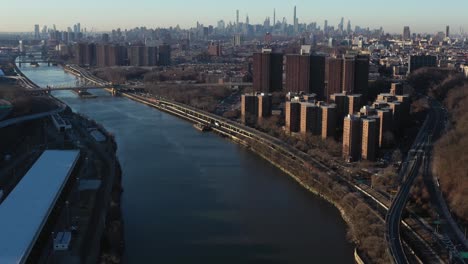 aerial footage glides down the harlem river of nyc between upper harlem and the south bronx, skyscrapers of midtown manhattan in the distance.