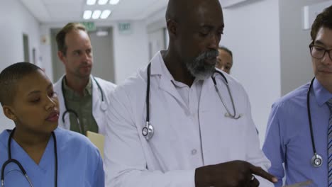 Diverse-group-of-male-and-female-doctors-walking-in-hospital-corridor-using-tablet-and-talking