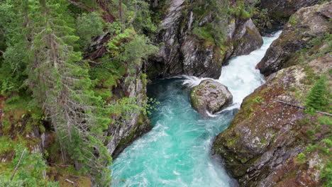 Aerial-view,-white-water-rapids-rushing-between-the-walls-of-a-craggy,-moss-covered-ravine