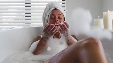 mujer afroamericana soplando burbujas de jabón en la bañera en el baño en casa