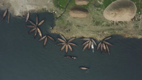 Luftaufnahme-Von-Holzbooten,-Die-In-Einem-Blumenmuster-Angeordnet-Sind-Und-Auf-Einem-Majestätischen-Fluss-Schwimmen