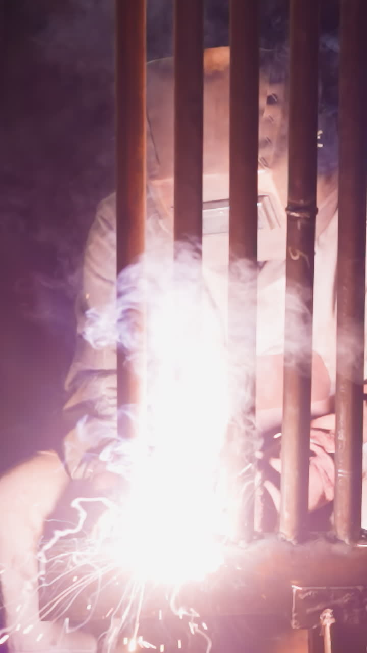 Employee welds steel pipeline grid for boiler room with flame in workshop slow motion. Professional worker connects metal tubes at metalworking plant