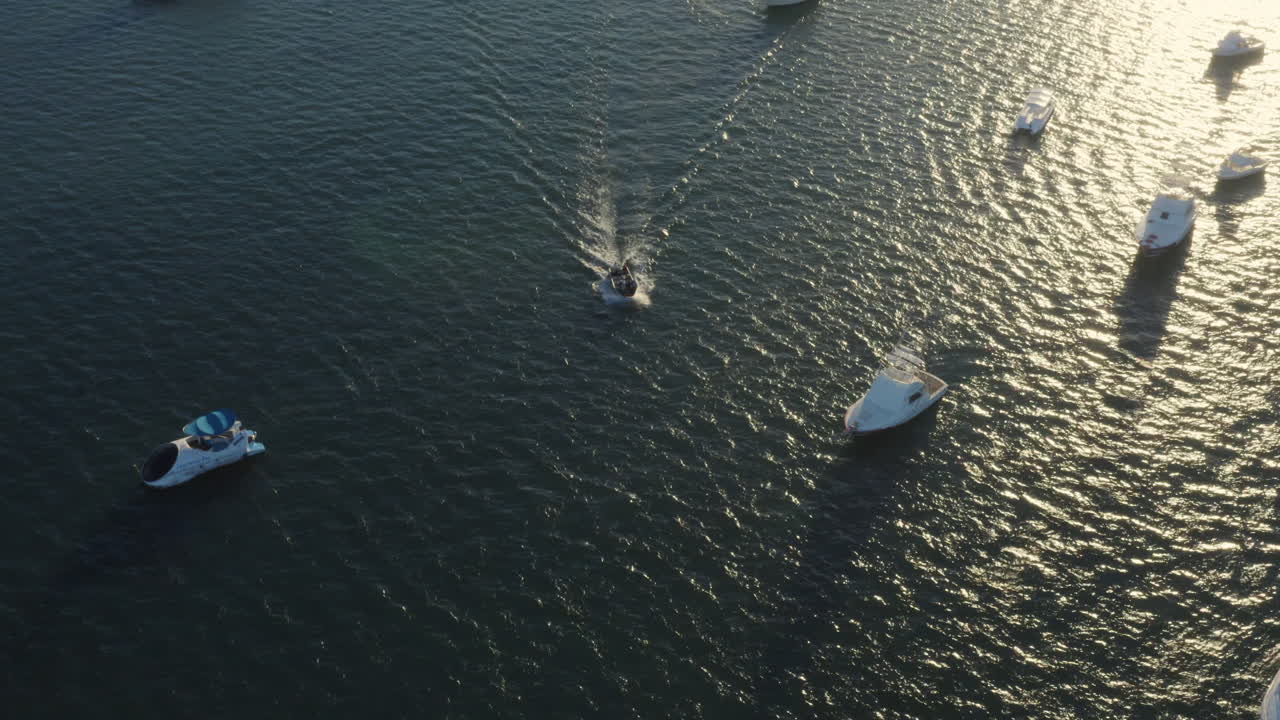 Goldene Sonne spiegelt sich, während ein kleines Boot zwischen geankerten Fischerbooten kreuzt, Punta Cana, Luftaufnahme (Schwenk nach unten).