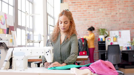 Diseñadora-De-Moda-Birracial-Cosiendo-Tela-Con-Máquina-De-Coser-En-Estudio,-Cámara-Lenta