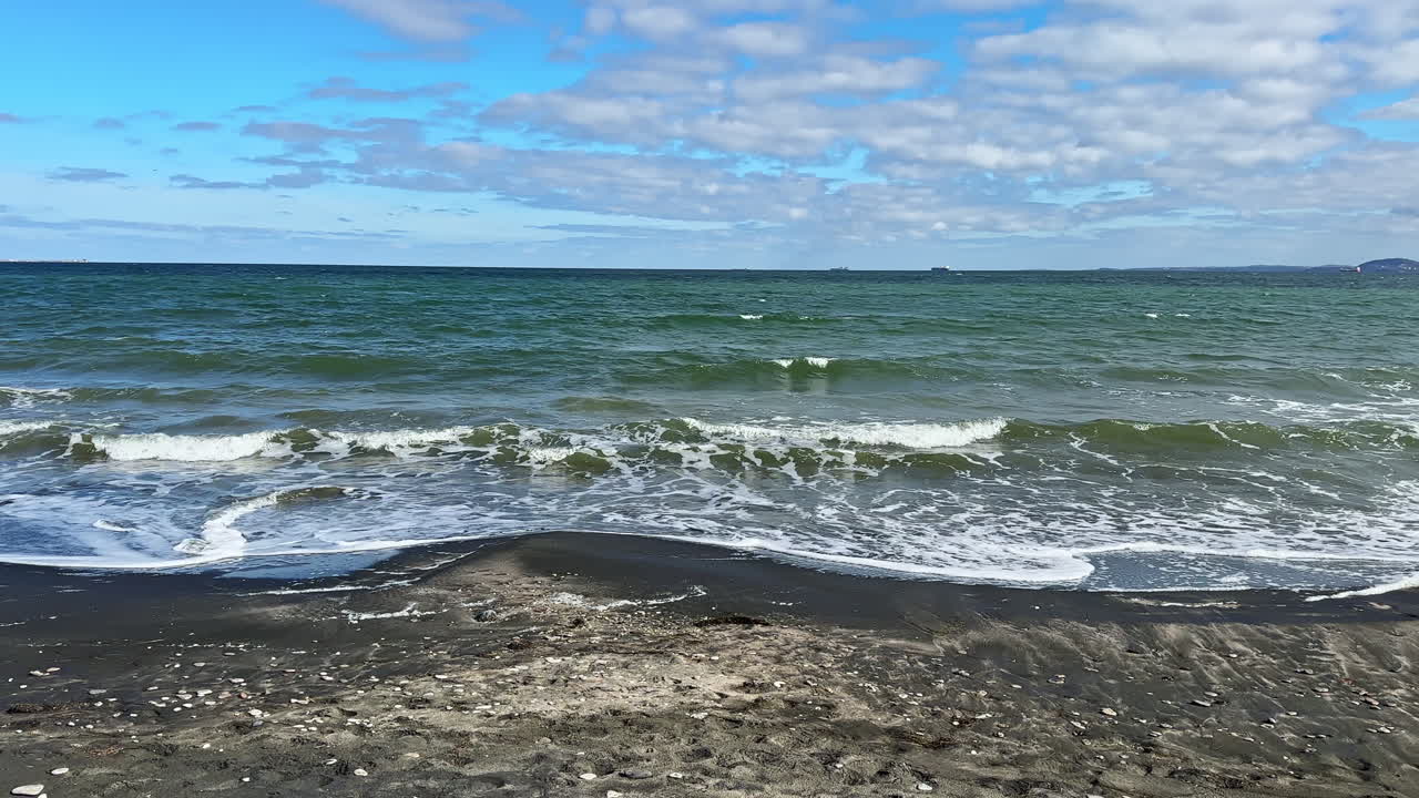 Vista di una spiaggia con onde e nuvole sull'acqua, scattata di giorno vicino a una zona costiera.