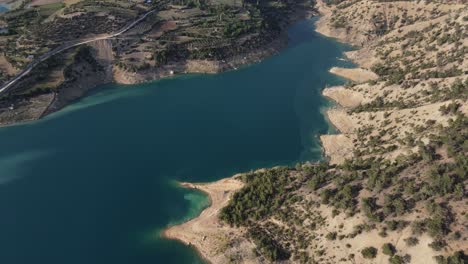 The-view-of-the-dam-in-the-mountains-taken-with-a-drone,-the-aerial-picture-of-the-large-water-lake,-dam-in-the-middle-of-green-fields