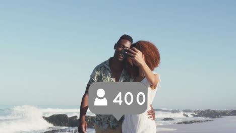 Profile-icons-with-increasing-numbers-against-african-american-couple-taking-a-selfie-on-the-beach