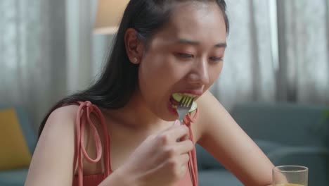 건강한 음식과 오렌지 주스 한 잔을 가진 아시아 여성의 근접 사진. 집에서 먹기 전에 오징어를 르는 포크를 사용합니다.