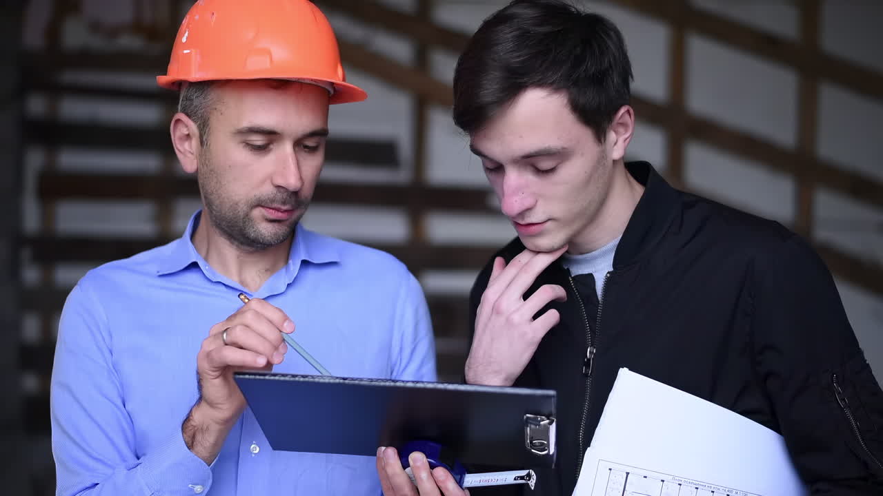 A site manager wearing an orange safety helmet explaining plans to a colleague on a construction site