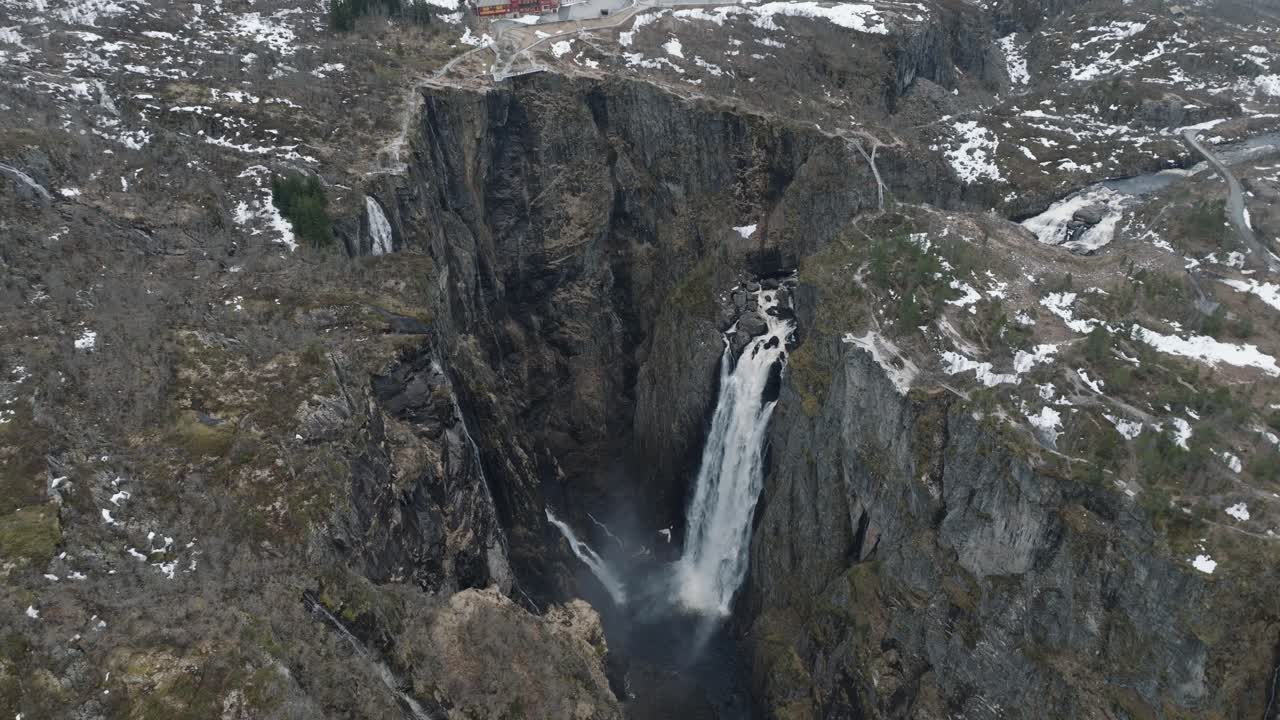 Drone Shot of Waterfall and Glacial River Canyon Under Snow Capped Hills and Ice Fields in Landscape of Norway
