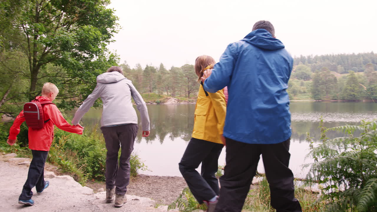 Ung familie går til en innsjø og leker ved strandkanten, sett bakfra, Lake District, Storbritannia.