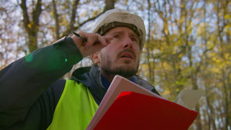 ingeniero masculino mirando hacia arriba a los árboles y leyendo en el clipboard en el medio del bosque, handheld closeup