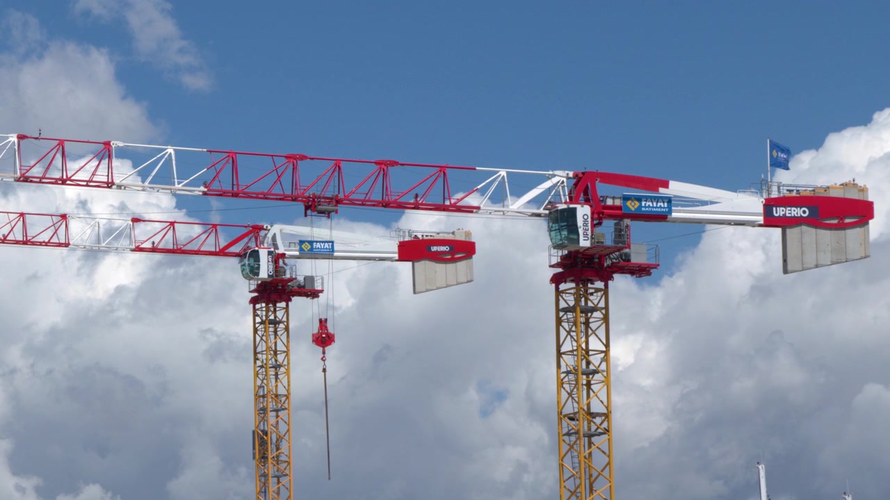 Cảnh quay tĩnh góc rộng những cần cẩu xây dựng màu đỏ và trắng nổi bật trên nền mây sáng và bầu trời xanh