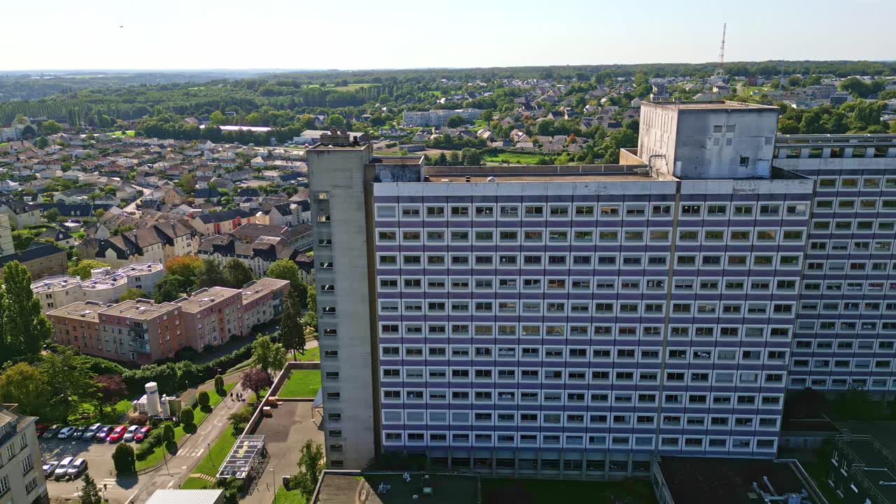 Tall hospital tower in Laval surrounded by trees and urban landscape under blue sky, aerial tracking