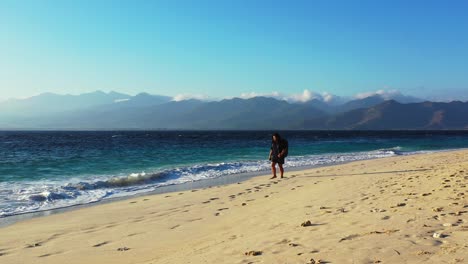 Touristische-Frau-Mit-Rucksack,-Die-Gerade-In-Den-Urlaub-Kommt-Und-Entlang-Des-Exotischen-Strandes-Spaziert,-Der-Vom-Blauen-Meer-In-Bali-Beeindruckt-Ist