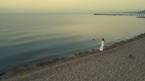 Beautiful-woman-in-white-dress-enjoys-lonely-walk-near-beach,aerial-view