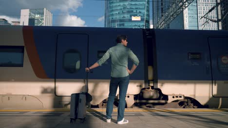 man with suitcase waiting at train station