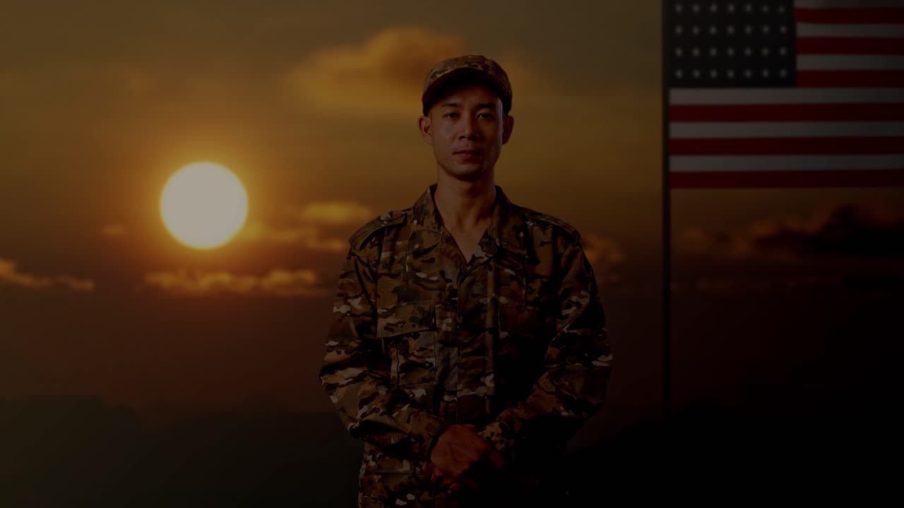 동양인 군인이 서서 미국 발을 들고 카메라를 바라보며, 해가 지는 시간