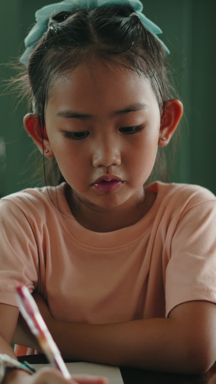 Giovane ragazza asiatica concentrata a scrivere o disegnare con una penna