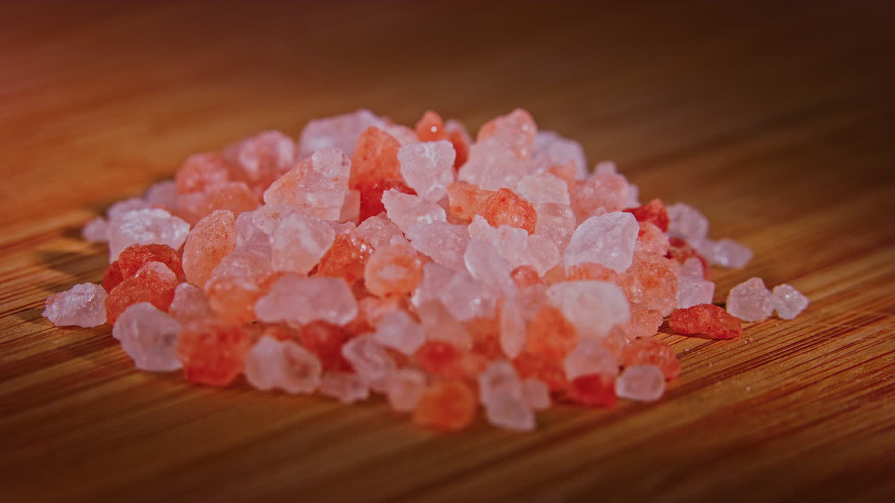 una pila de sal rosa del himalaya en una superficie de madera con iluminación dramática, cámara en órbita