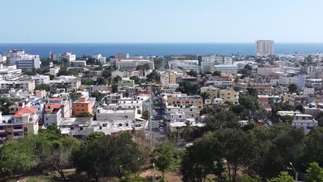 Toma-Aérea-Con-Drone-Pasando-El-Mirador-Sur-Y-Mostrando-La-Zona-Del-Barrio-En-Los-Jardines-Del-Sur,-Santo-Domingo