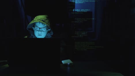 genius boy hacker working on laptop computer in the dark with overlaying programming codes. zoom-in